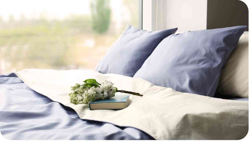 a blue comforter on a bed next to a book and a bouquet of flowers